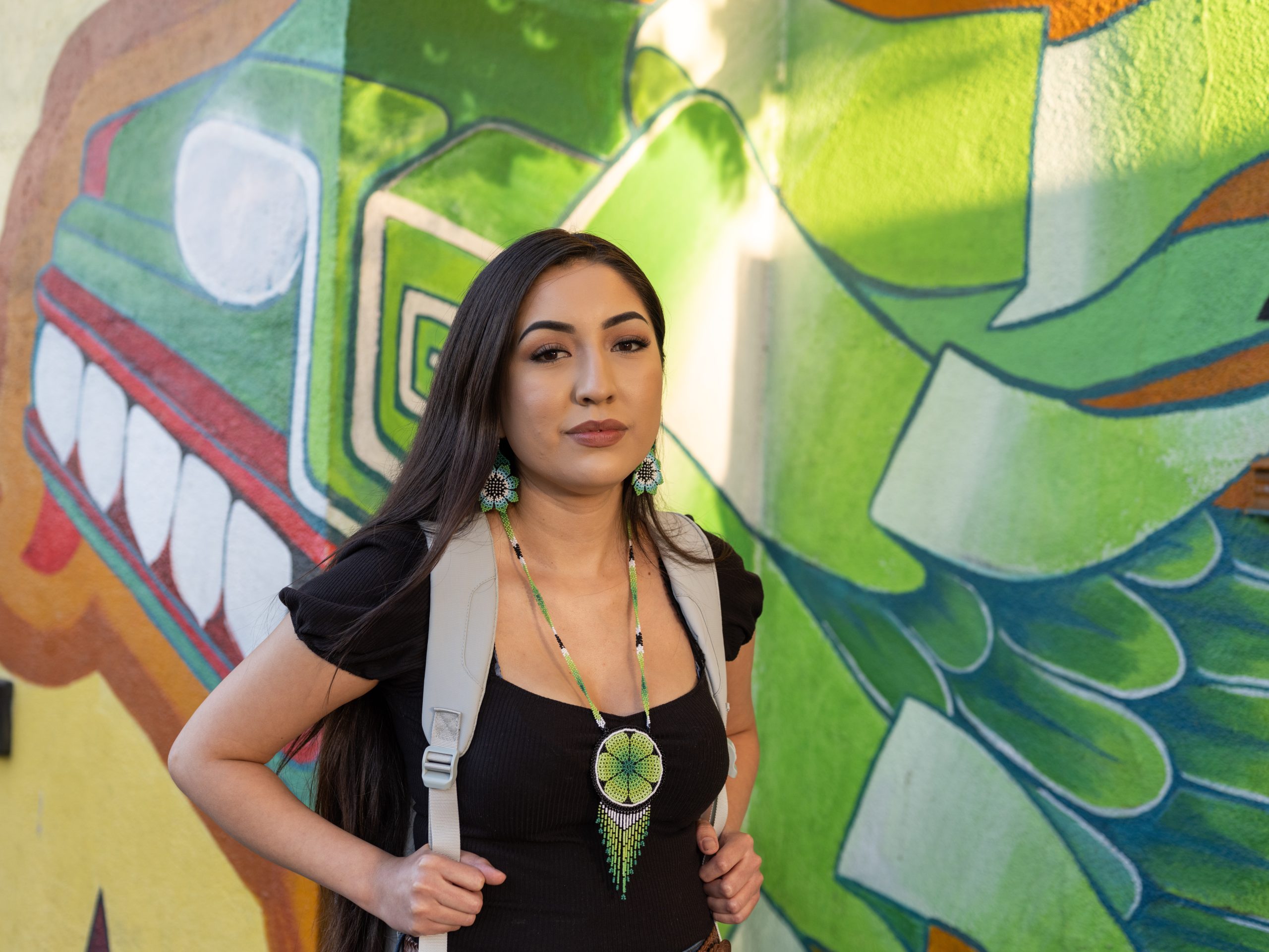 A woman with a backpack is standing in front of a mural.